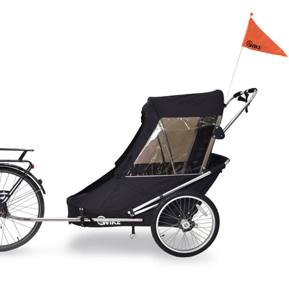 A black Wike Special Needs Large Bike Trailer with a retractable canopy, attached to a bicycle, equipped with a stroller and jogging kit, including a safety flag and spoked alloy wheels.